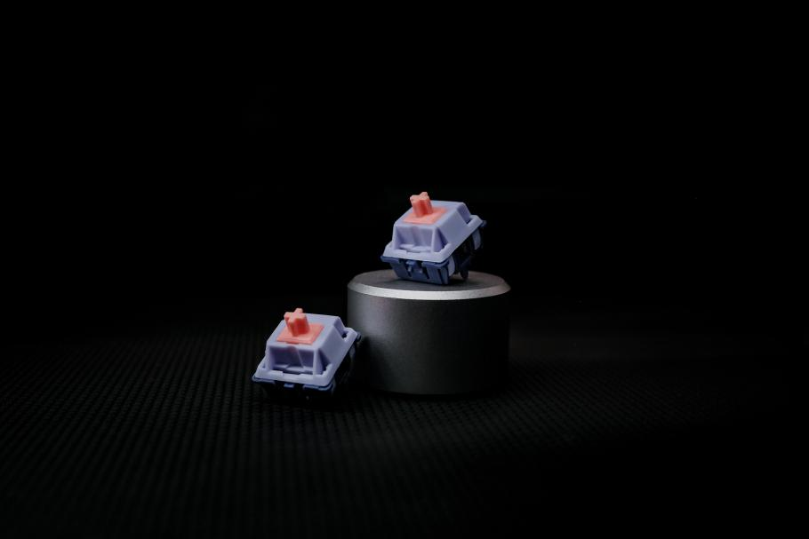 Close-up shot of two Commute mechanical keyboard switches with one on a small display stand with a black background and dim lighting