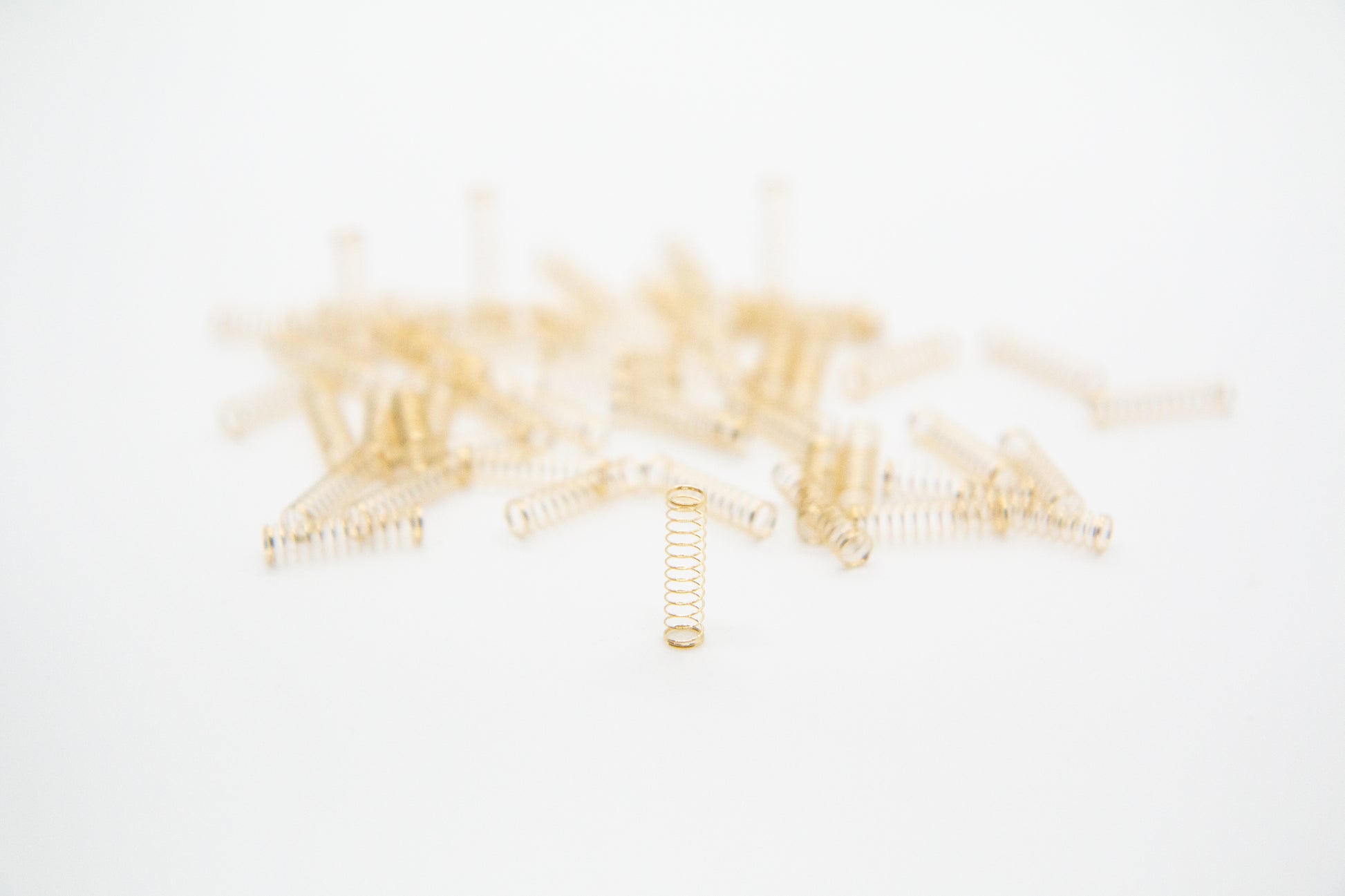 Close-up shot of a single 78g dual stage gold plated mechanical keyboard spring on a grey background