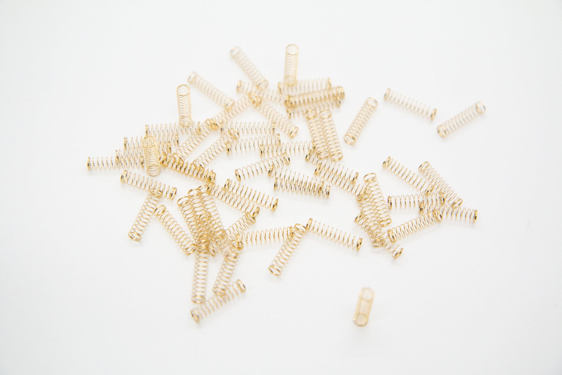 Close-up shot of a single 62g dual stage gold plated mechanical keyboard spring on a grey background
