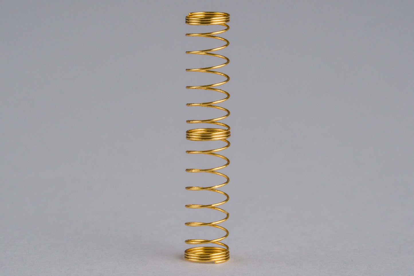 Close-up shot of a single 68g dual stage gold plated mechanical keyboard spring on a grey background