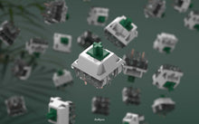 Load image into Gallery viewer, Close-up shot of a BBN Linear mechanical keyboard switch with an assortment of BBN Linear switches falling behind it with a green background and stringy plant leaves on the left
