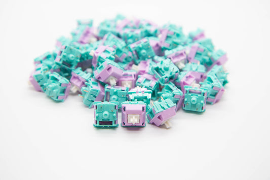 Close-up shot of a pile of Ethereal Panda mechanical keyboard switches featuring teal and purple housing and white stems