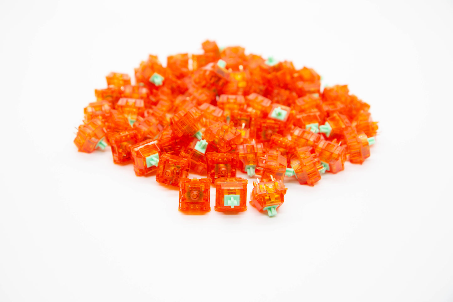 Close up shot of a pile Tangerine mechanical keyboard switches featuring orange semi-transparent housing and light green stems