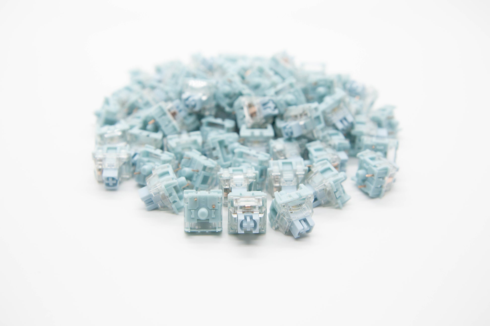 Close-up shot of a pile of TTC Bluish White mechanical keyboard switches featuring soft baby blue and transparent housing and soft blue stems