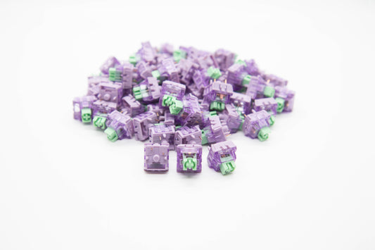 Close-up shot of a pile of Lupine mechanical keyboard switches featuring light purple housing and teal stems
