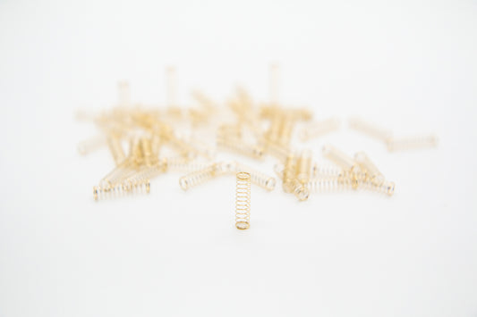 Close-up shot of a single 78g dual stage gold plated mechanical keyboard spring on a grey background