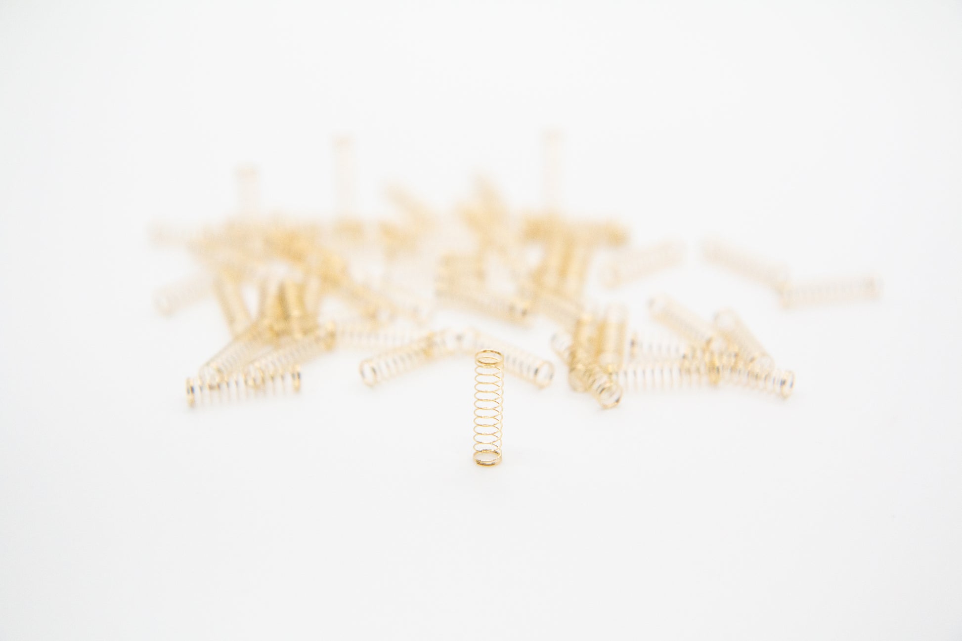 Close-up shot of a single 63.5g dual stage gold plated mechanical keyboard spring on a grey background