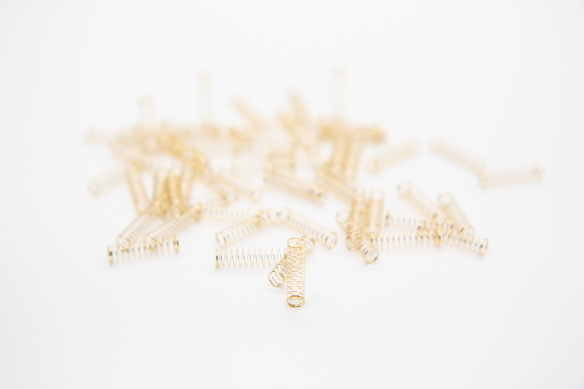 Close-up shot of a single 55g dual stage gold plated mechanical keyboard spring on a grey background