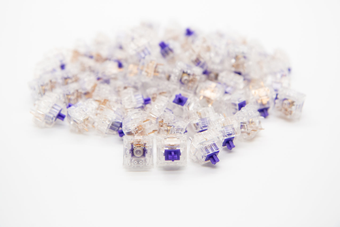 Close-up shot of a pile of ZealPC Zealios V2 - 65g mechanical keyboard switches featuring transparent housing and purple stems