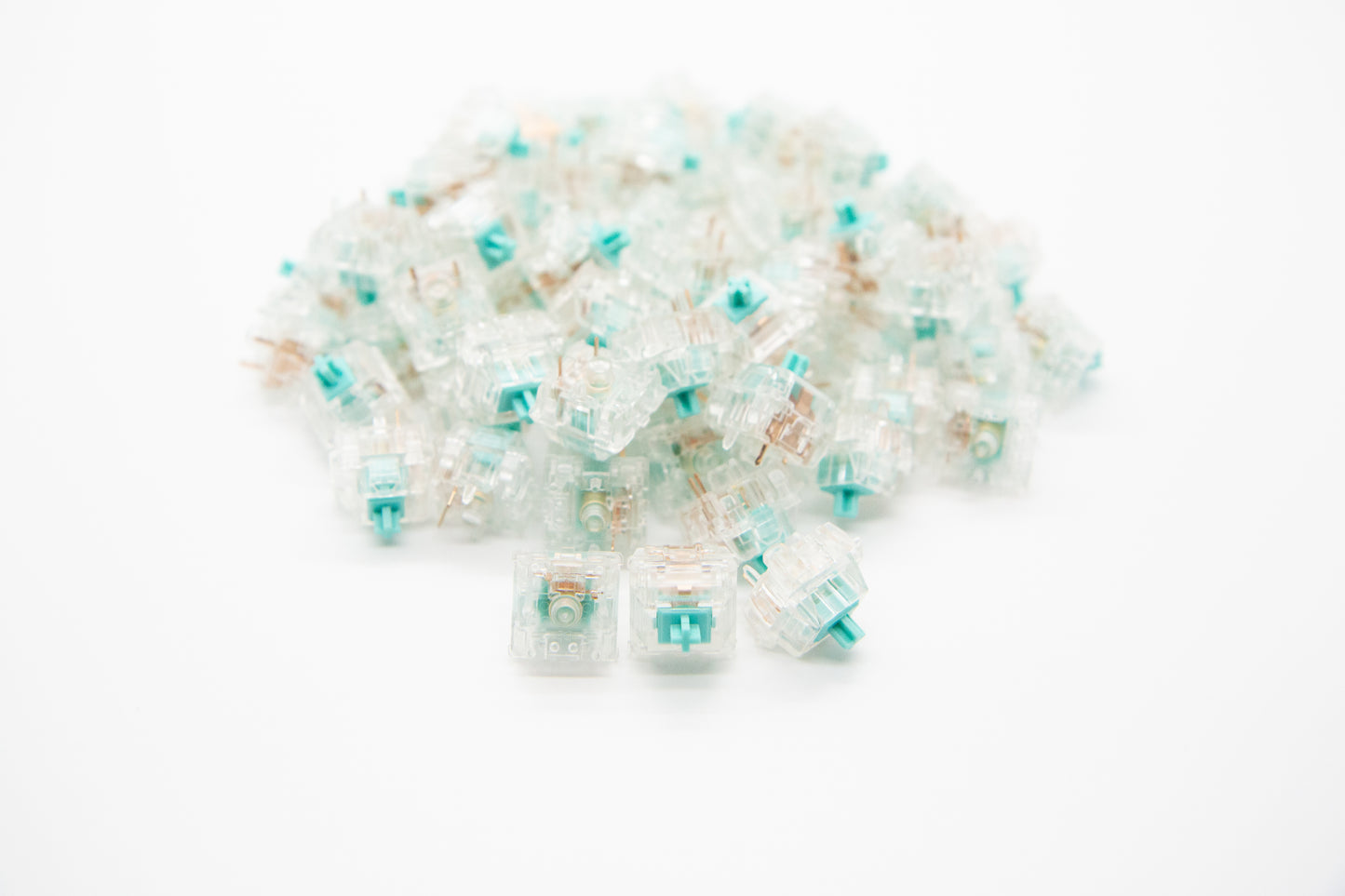 Close-up shot of a pile of ZealPC Tealios V2 - 67g mechanical keyboard switches featuring transparent housing and teal stems