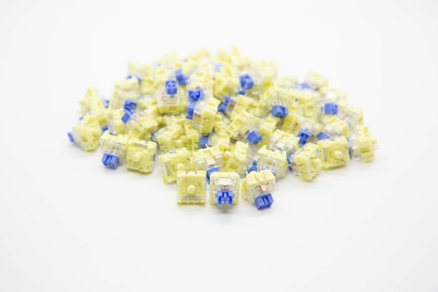 Close-up shot of a pile of TTC Golden Blue mechanical keyboard switches featuring yellow and transparent housing and blue stems